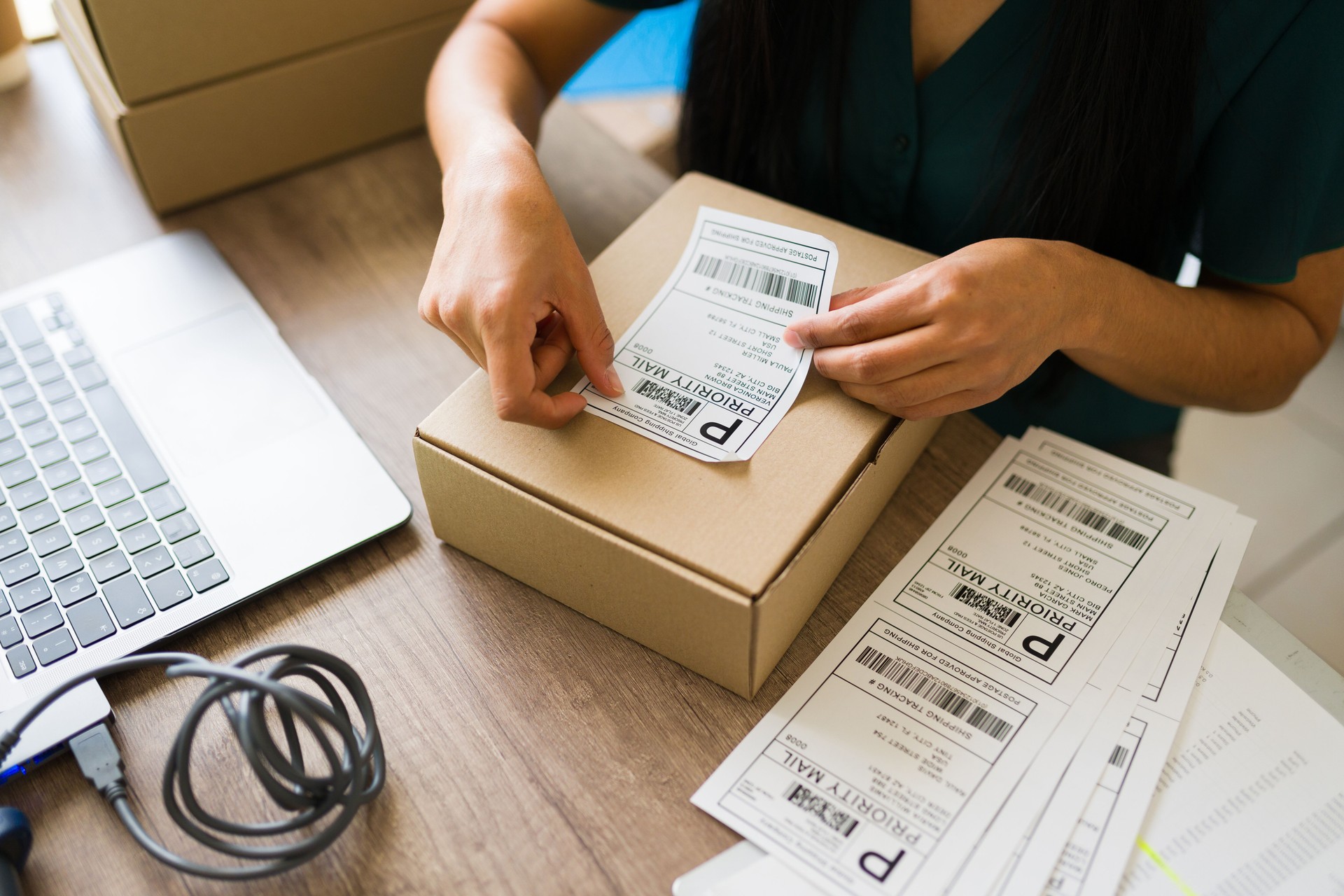 Closeup of a female business owner preparing a shipment, affixing a priority mail label to a cardboard box at her small business office Closeup of a female business owner preparing a shipment, affixing a priority mail label to a cardboard box at her small business office